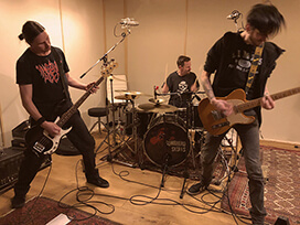 Schlagzeuger, Gitarrist und Bassist nehmen im großen Aufnahmeraum einen Song auf